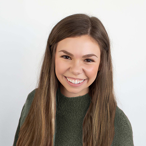 Woman with long, brown hair and dark green sweater smiles toward the camera