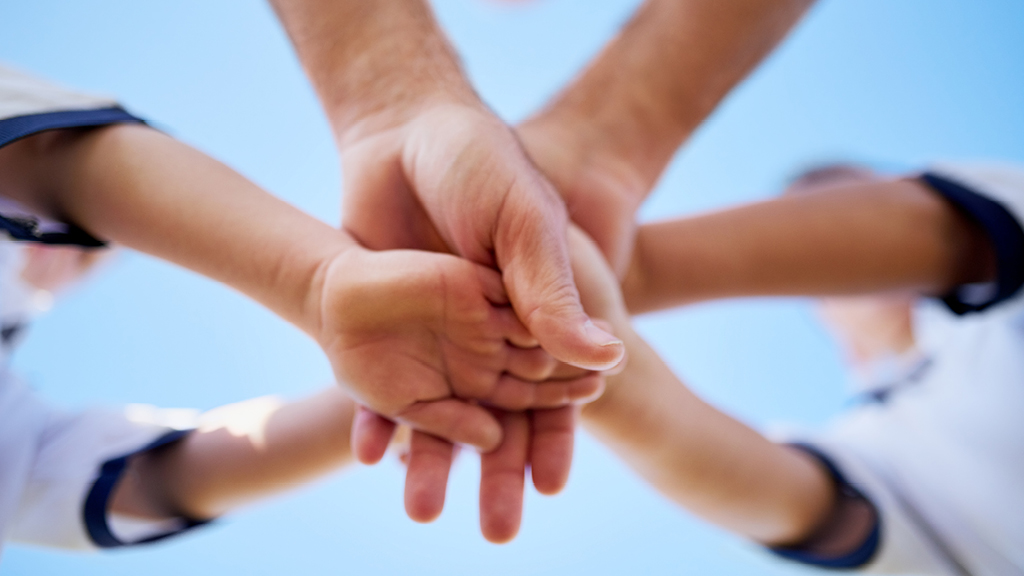 group of kids' and their leader's hands in a huddle