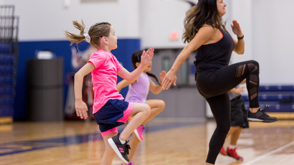 kids doing exercises in a gym with an adult leader