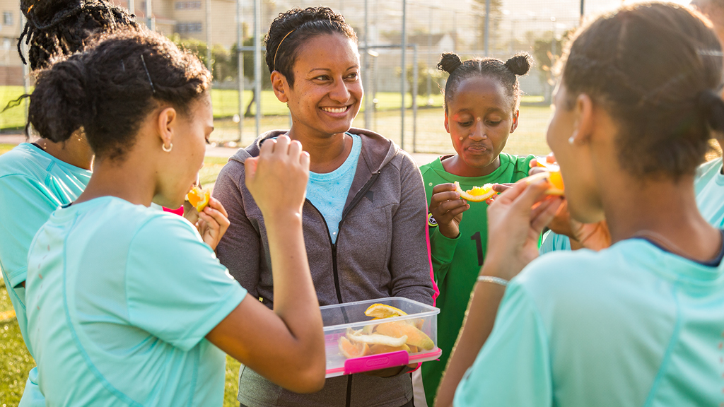 Group of kids standing outdoors and eating oranges