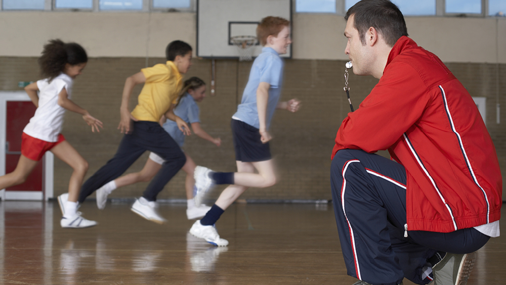 kids playing a game in a gym while adult watches
